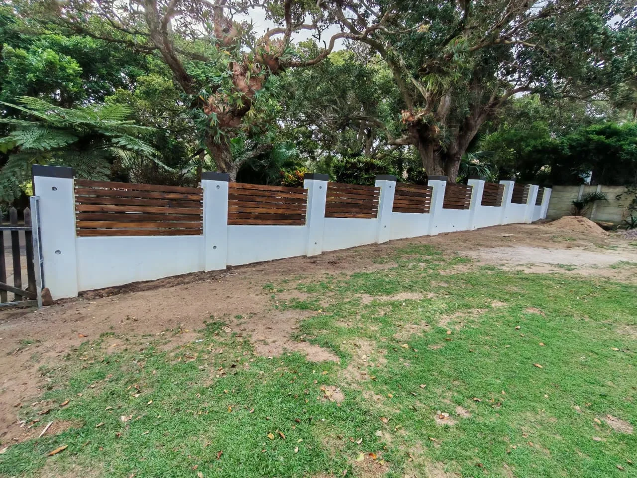 A long boundary fence with timber-look infill among established trees